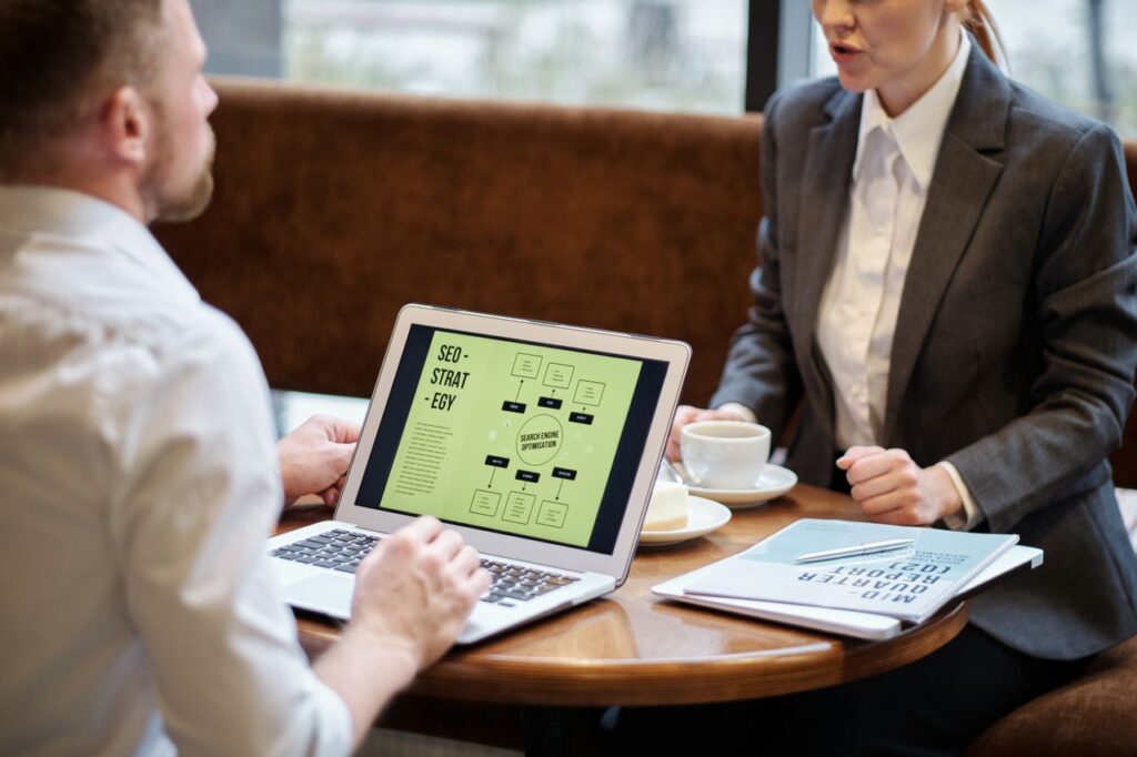 Services A man and woman engaged in a business meeting discussing SEO strategy in a cozy cafe setting.
